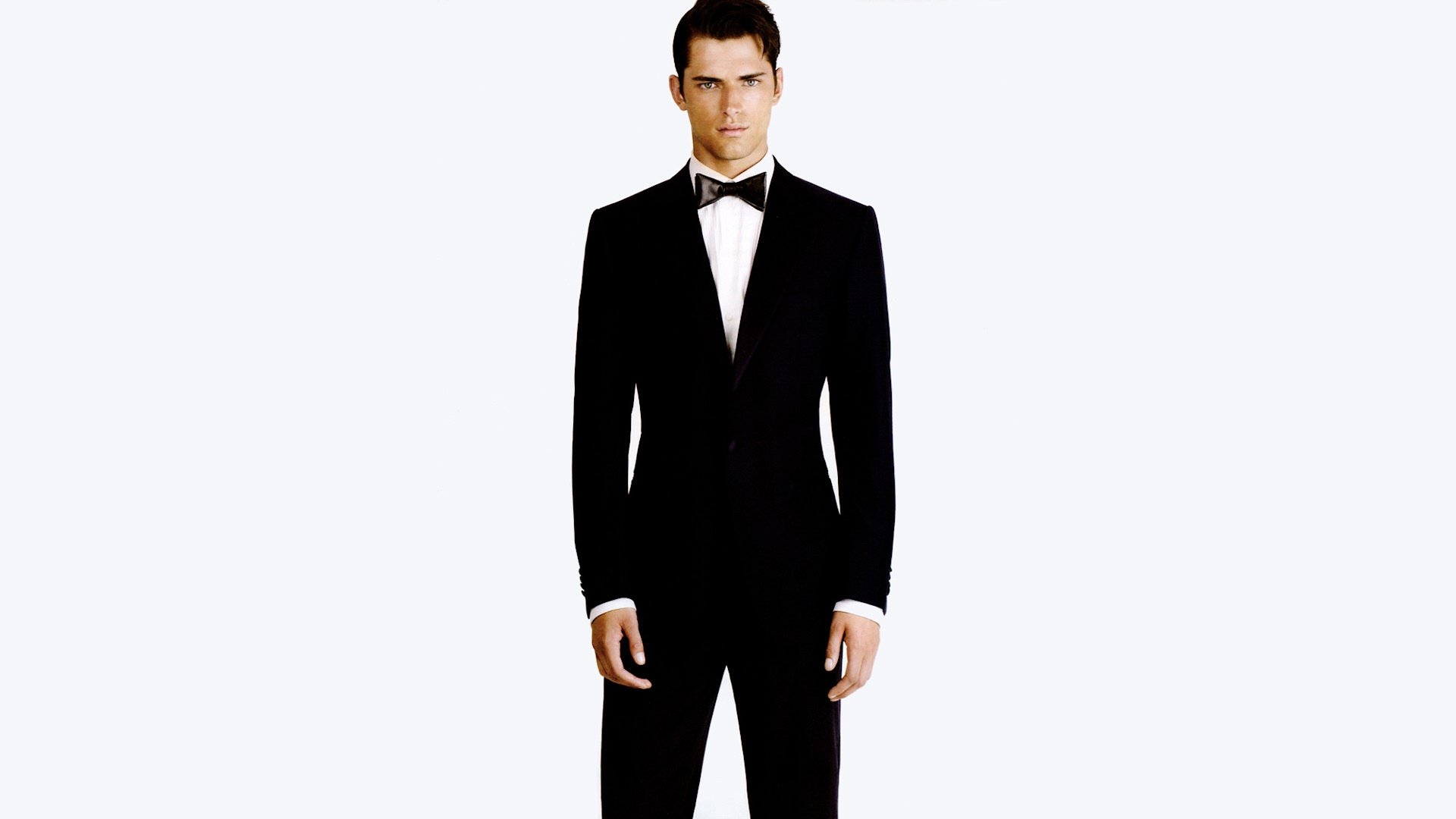 HD wallpaper featuring a man in a black tuxedo standing against a plain white background, exuding elegance and sophistication.