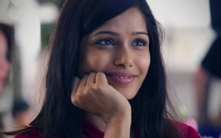 A captivating HD desktop wallpaper featuring Freida Pinto, showcasing her warm smile and thoughtful expression. The image captures her charm and presence beautifully.