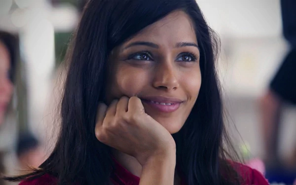 A captivating HD desktop wallpaper featuring Freida Pinto, showcasing her warm smile and thoughtful expression. The image captures her charm and presence beautifully.