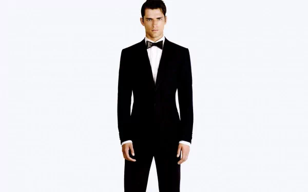 HD wallpaper featuring a man in a black tuxedo standing against a plain white background, exuding elegance and sophistication.
