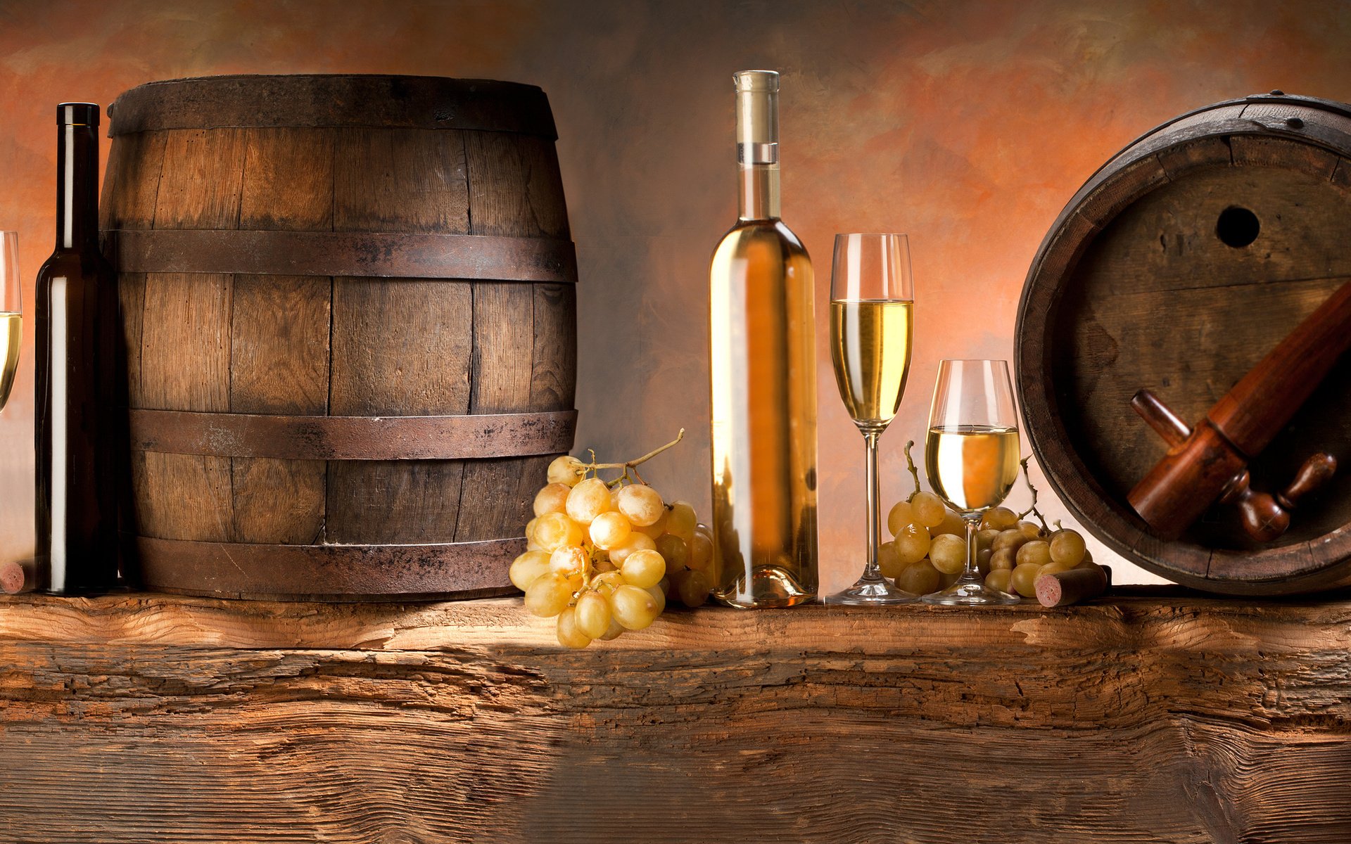 HD PC desktop wallpaper featuring a rustic food and wine setting with wooden barrels, white wine bottles, glasses, and fresh grapes on a wooden surface.