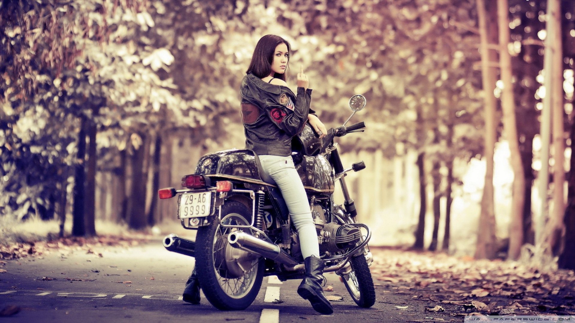 A woman in a leather jacket sits on a parked motorcycle on a tree-lined road; an HD PC desktop wallpaper featuring a stylish vehicle and motorcycle scene.