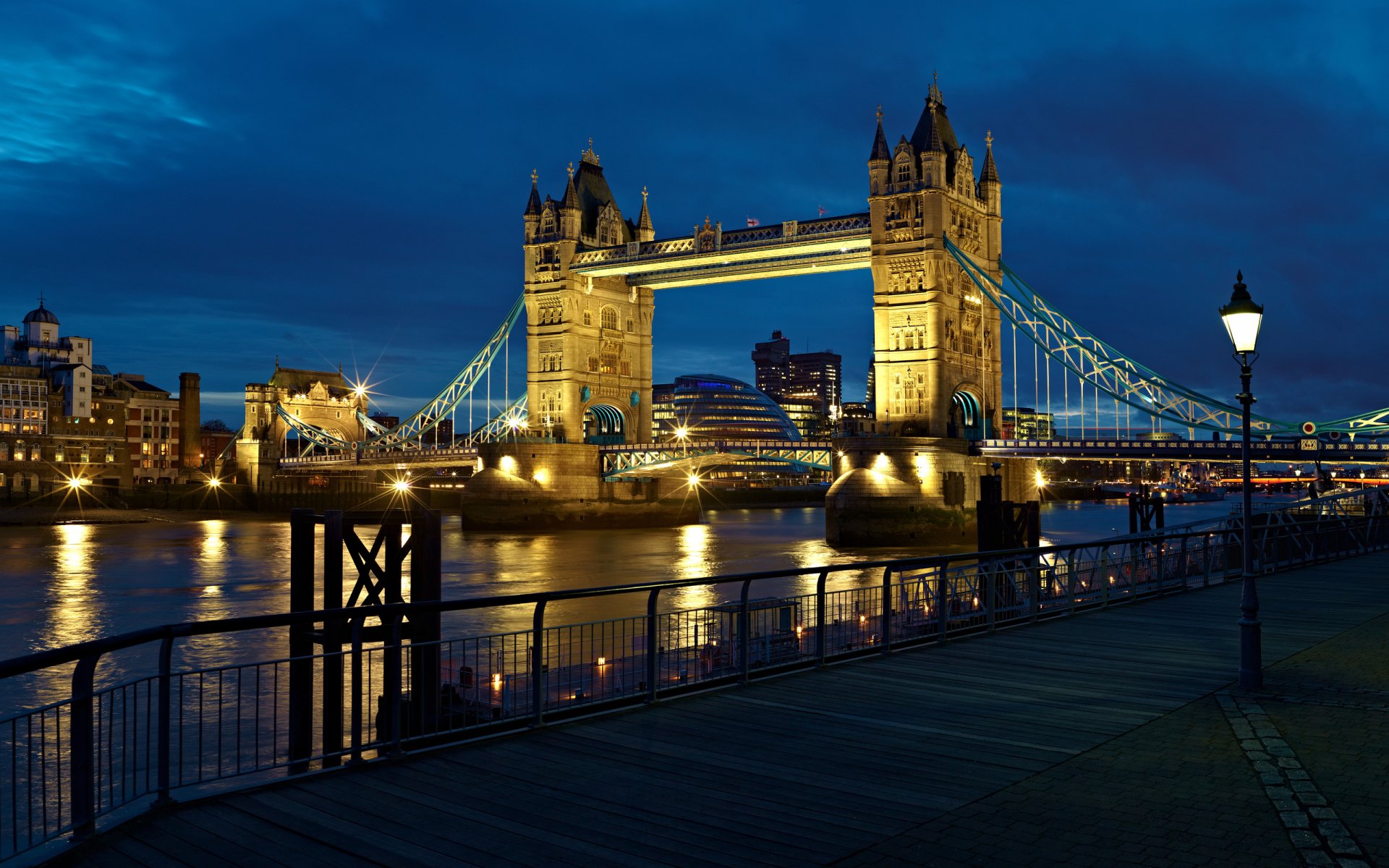 HD desktop wallpaper featuring the illuminated Tower Bridge at night, showcasing its iconic man-made architecture against a deep blue sky.