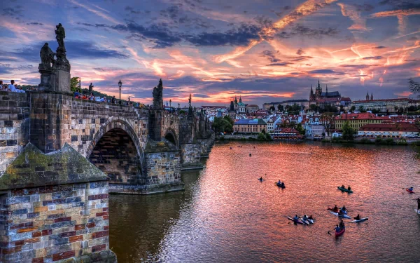 HD desktop wallpaper showcasing the historic Charles Bridge and Prague skyline at sunset with boats on the Vltava River.
