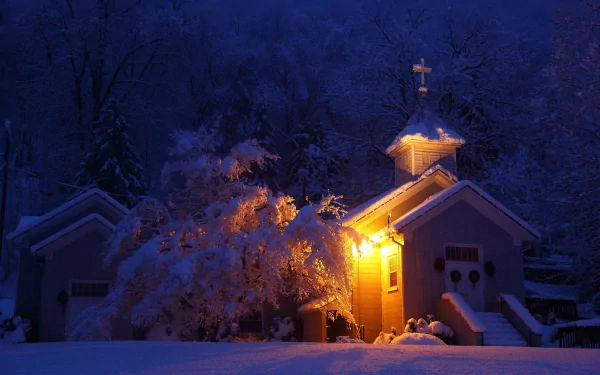 HD PC desktop wallpaper showing a softly illuminated church at night, surrounded by snow-covered trees in a serene, religious winter scene.