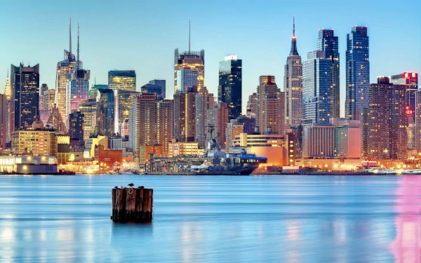A stunning view of Manhattan's skyline at dusk, showcasing the vibrant man-made structures of New York, with reflections shimmering on the water. Ideal HD desktop wallpaper.