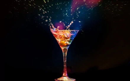 HD desktop wallpaper of a colorful cocktail splashing with vibrant liquid and fruit against a dark background, highlighting dynamic motion and vivid colors.
