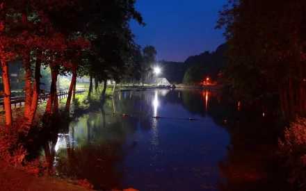 A serene park scene at night, featuring a calm lake surrounded by trees and illuminated by soft lights, creating a tranquil atmosphere for an HD desktop wallpaper.