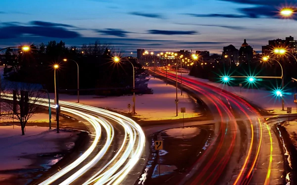 Photography time-lapse of a dusk urban highway with sweeping car light trails and glowing streetlights — 2K Quad HD PC desktop wallpaper and background.