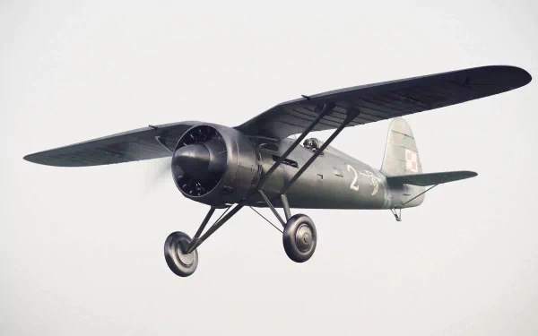 Military PZL P.11 fighter in olive drab, front three-quarter view in flight against a pale sky — 4K Ultra HD PC desktop wallpaper and background.