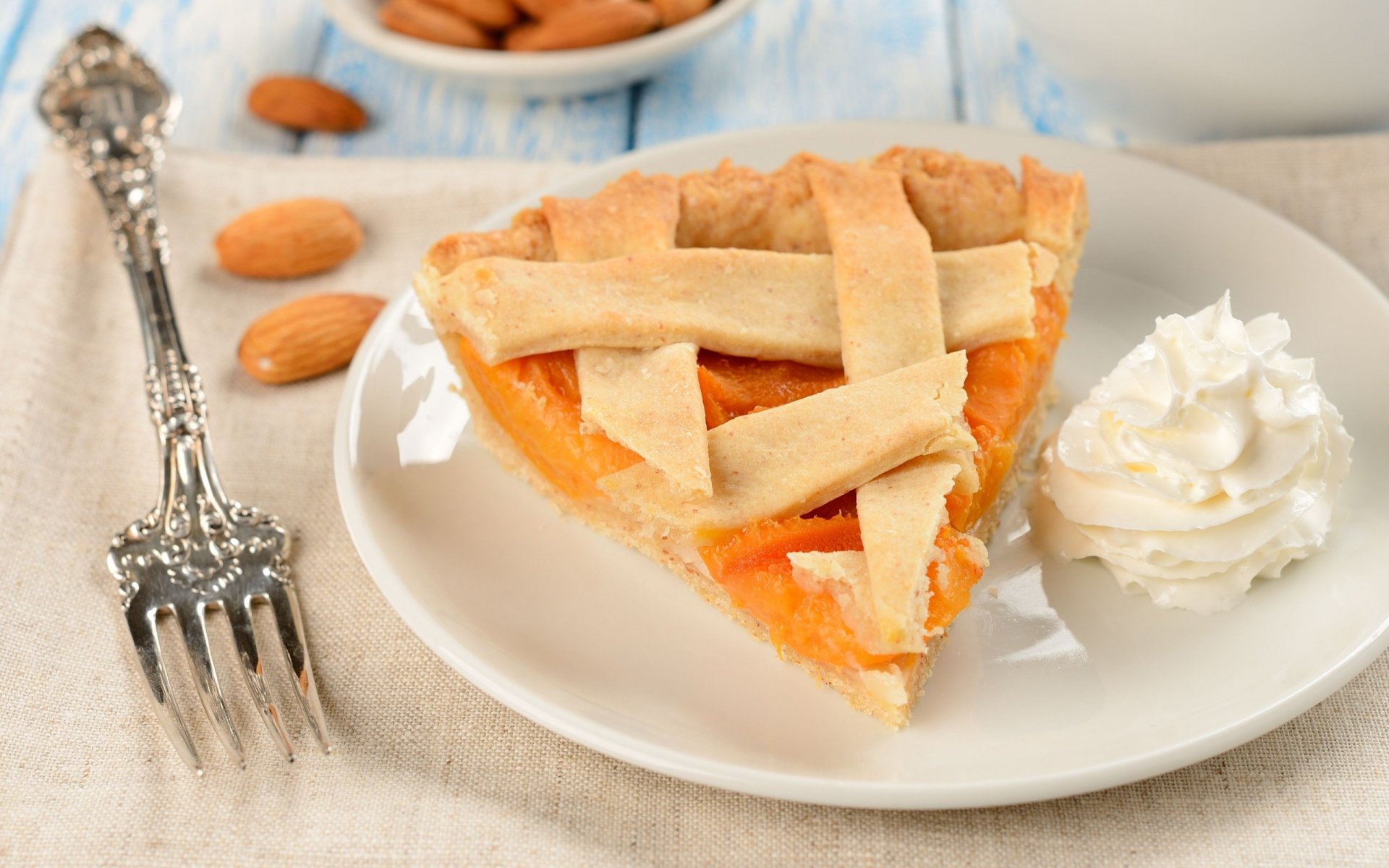 A delicious slice of cake with a golden crust, served with whipped cream, surrounded by almonds, creating a tempting food-themed HD desktop wallpaper and background.