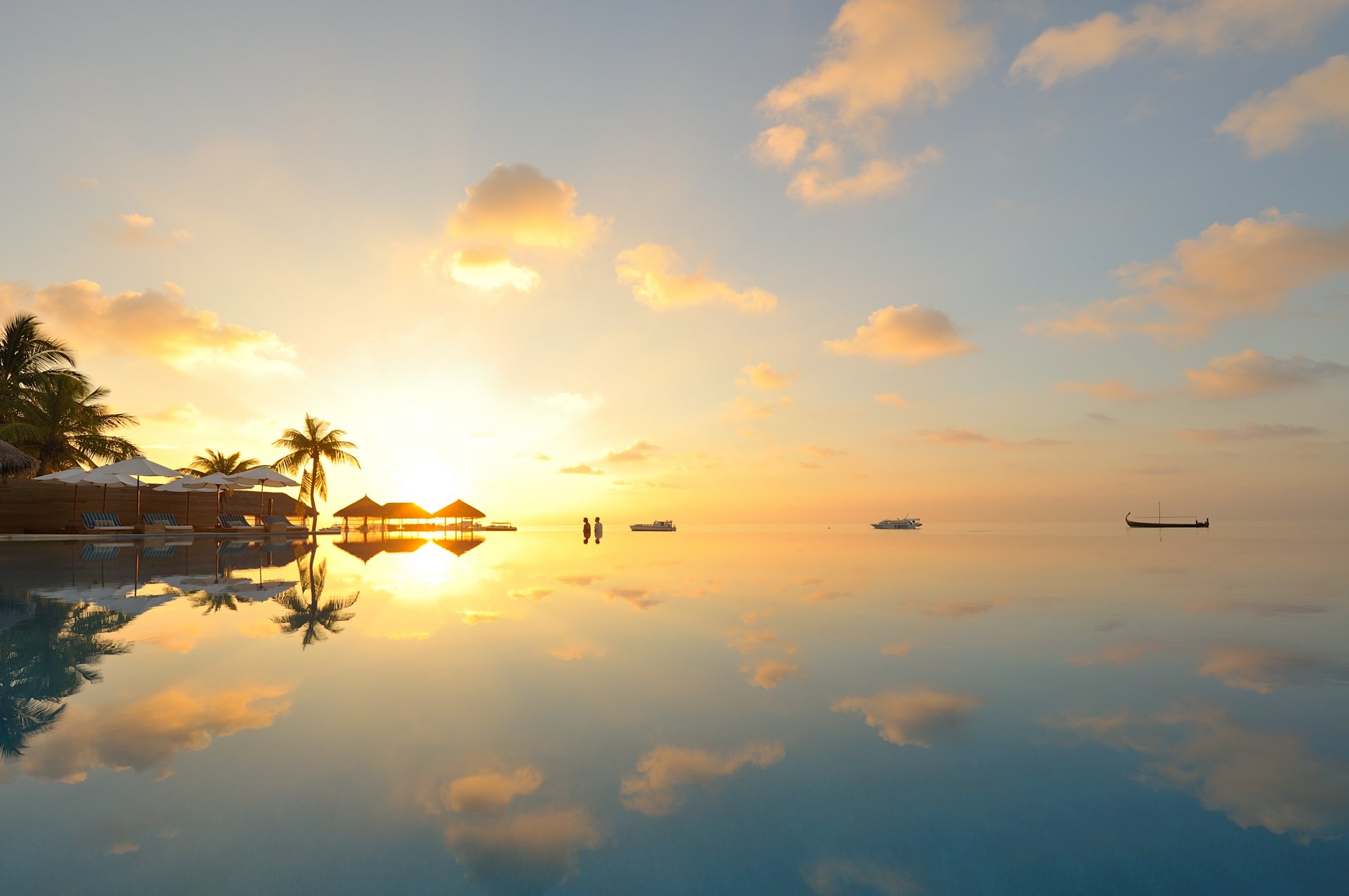 4K Ultra HD desktop wallpaper featuring serene photography of a tropical sunrise with calm water perfectly reflecting palm trees and boats under a partly cloudy sky.