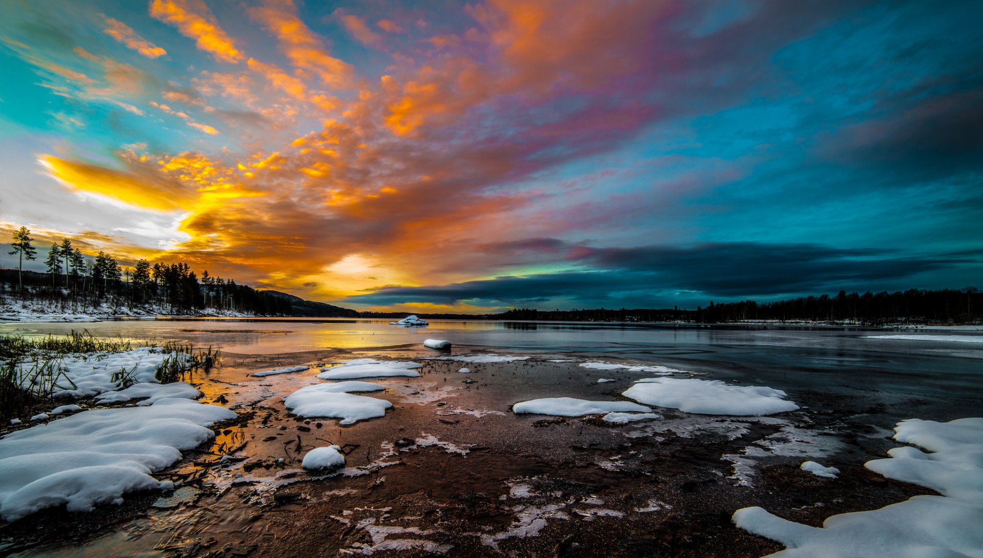 HD nature desktop wallpaper showcasing a vibrant sunset over a partially frozen lake with snow patches and silhouetted trees under a colorful sky.