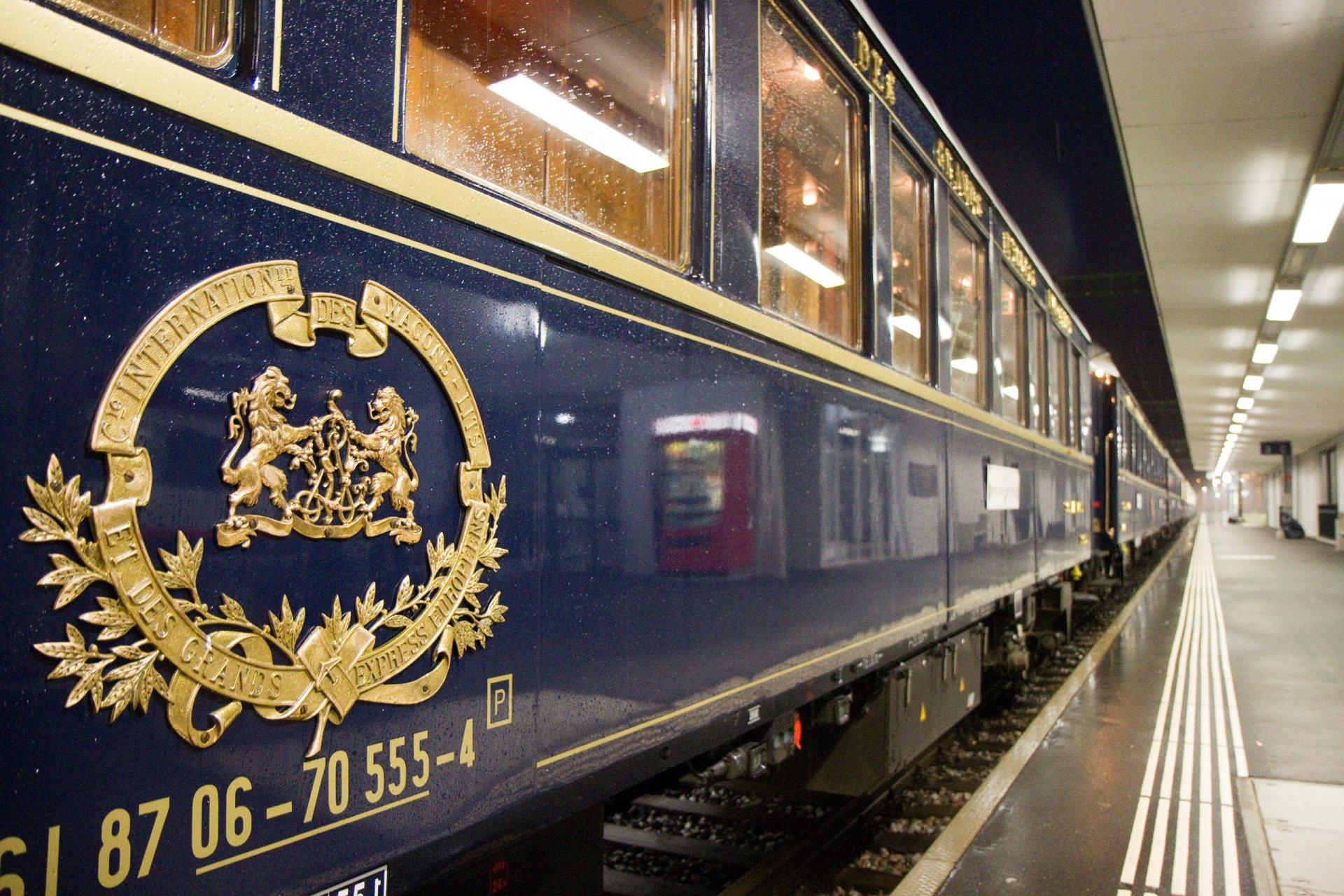 Photography: vintage blue luxury train carriage with gold crest at a well-lit station platform, reflective exterior and glowing windows — HD PC desktop wallpaper and background.
