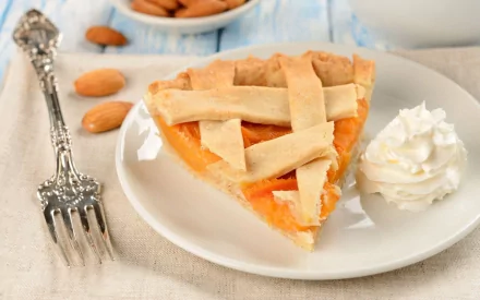 A delicious slice of cake with a golden crust, served with whipped cream, surrounded by almonds, creating a tempting food-themed HD desktop wallpaper and background.