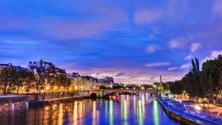 A serene view of the Seine River in Paris, capturing the vibrant city lights shimmering on the water under a twilight sky. An HD wallpaper showcasing the beauty of this man-made landscape.