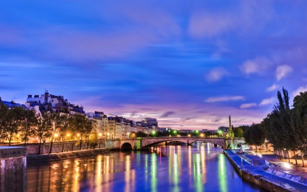 A serene view of the Seine River in Paris, capturing the vibrant city lights shimmering on the water under a twilight sky. An HD wallpaper showcasing the beauty of this man-made landscape.