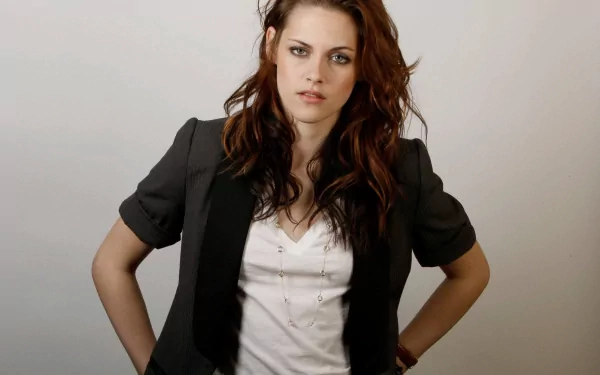 HD desktop wallpaper featuring celebrity Kristen Stewart. She stands with hands on hips, wearing a grey blazer over a white shirt, with a neutral expression against a plain background.