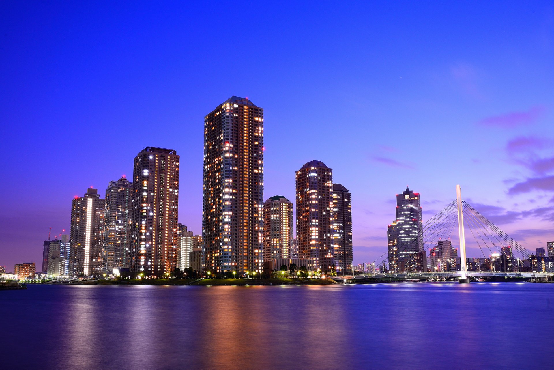 A vibrant Tokyo skyline at dusk, featuring modern skyscrapers illuminated against a purple sky, reflecting on the calm waters—a stunning HD desktop wallpaper.