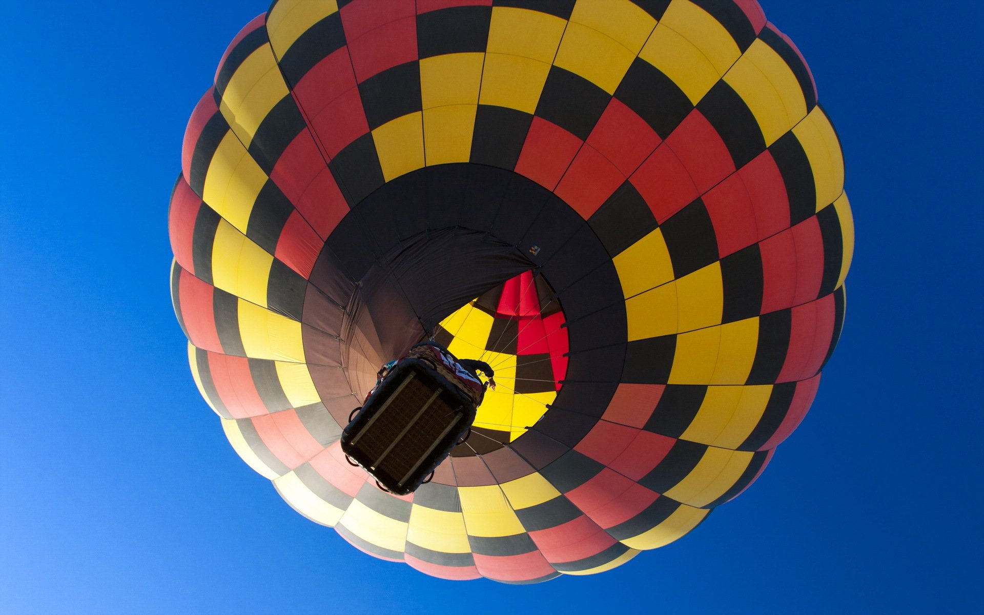Vibrant hot air balloon with red, yellow, and black checker pattern ascending against a clear blue sky, captured in HD for a stunning PC desktop wallpaper.