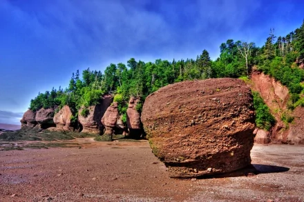 HD PC desktop wallpaper showing large rounded rock formations along a forested shoreline under a bright blue sky.