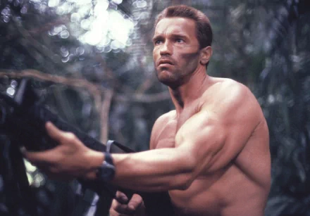Arnold Schwarzenegger, from the movie Predator, stands in a jungle setting with a determined look and a weapon in hand. HD desktop wallpaper and background.