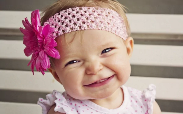 HD photography of a smiling baby girl wearing a pink crocheted headband with a large flower, sitting against a neutral background, captured as a desktop wallpaper.