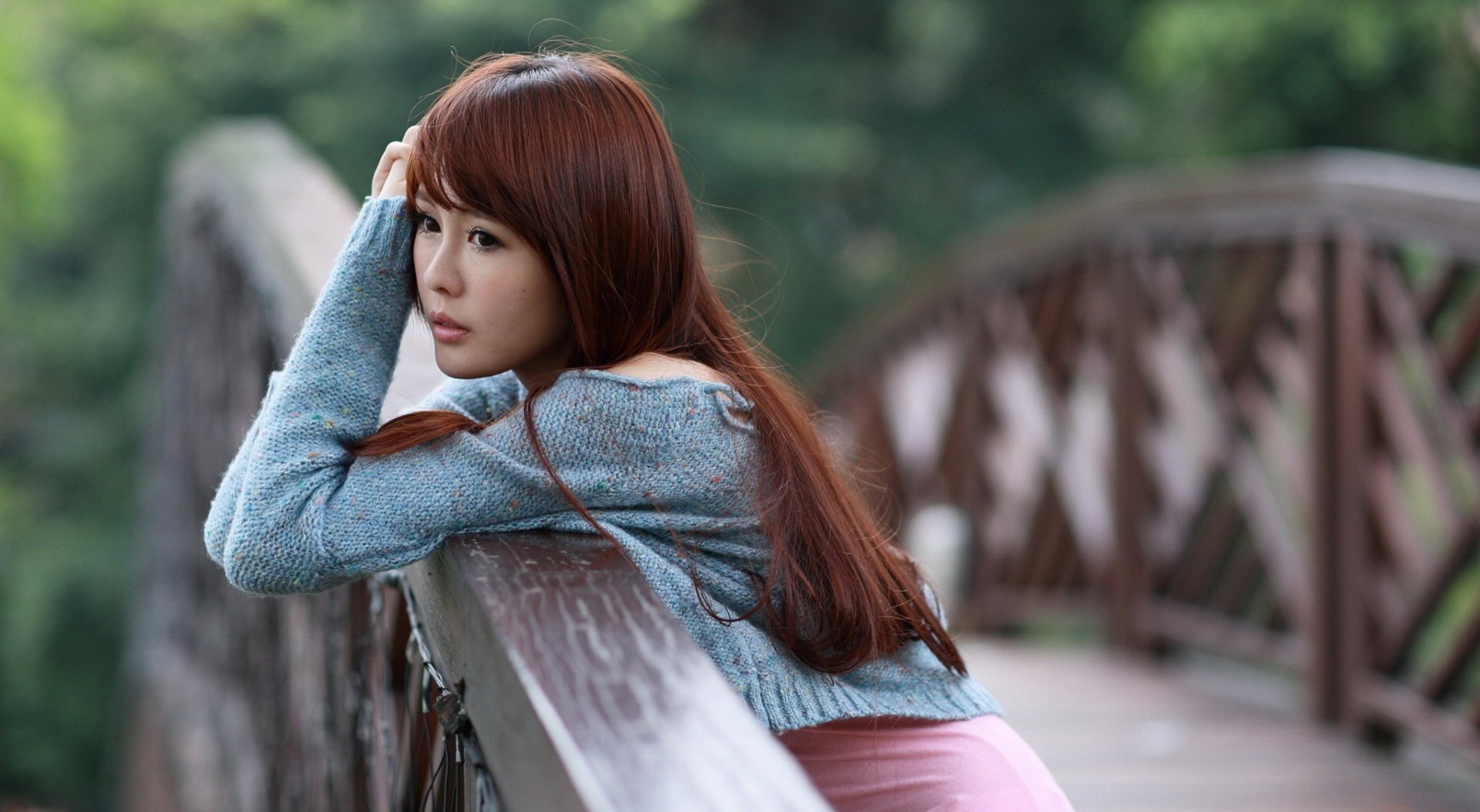 An Asian woman leans on a rustic wooden bridge, gazing thoughtfully into the distance. The background is lush and green, creating a serene and peaceful HD desktop wallpaper and background.