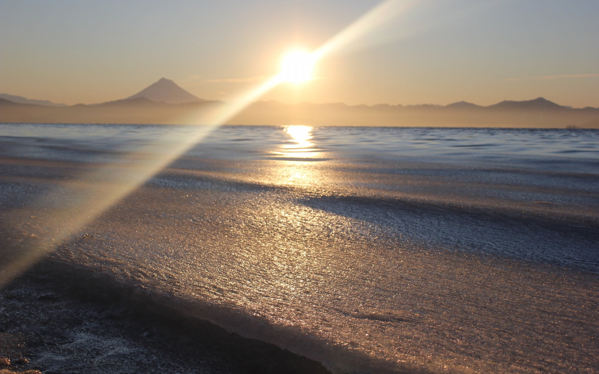 HD PC desktop wallpaper showcasing a serene ocean scene with gentle waves and a glowing sunrise over distant mountains in a natural setting.