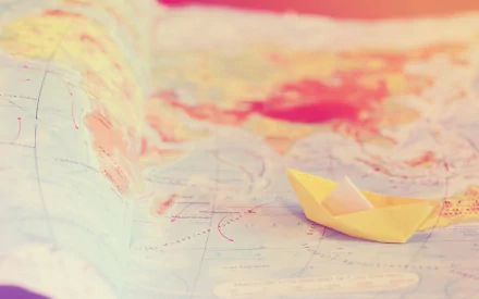 HD desktop wallpaper featuring a man-made origami paper boat resting on a softly blurred map background.