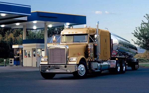 HD desktop wallpaper featuring a gold Freightliner truck parked at a gas station under clear blue skies.