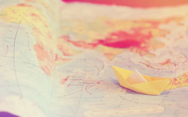 HD desktop wallpaper featuring a man-made origami paper boat resting on a softly blurred map background.