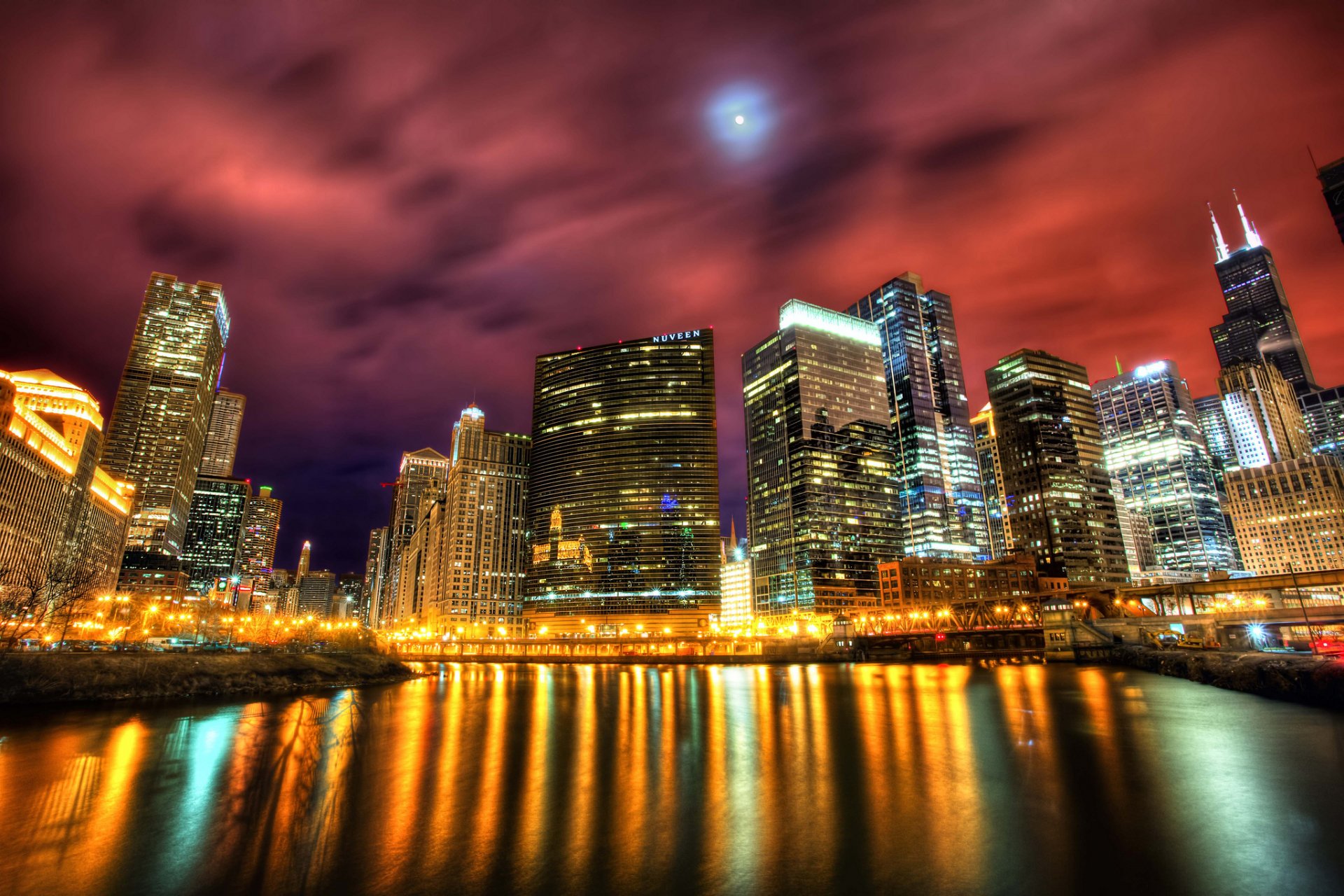 HD desktop wallpaper showcasing Chicago's man-made skyline at night with illuminated buildings reflecting on the river under a dramatic red and purple sky.