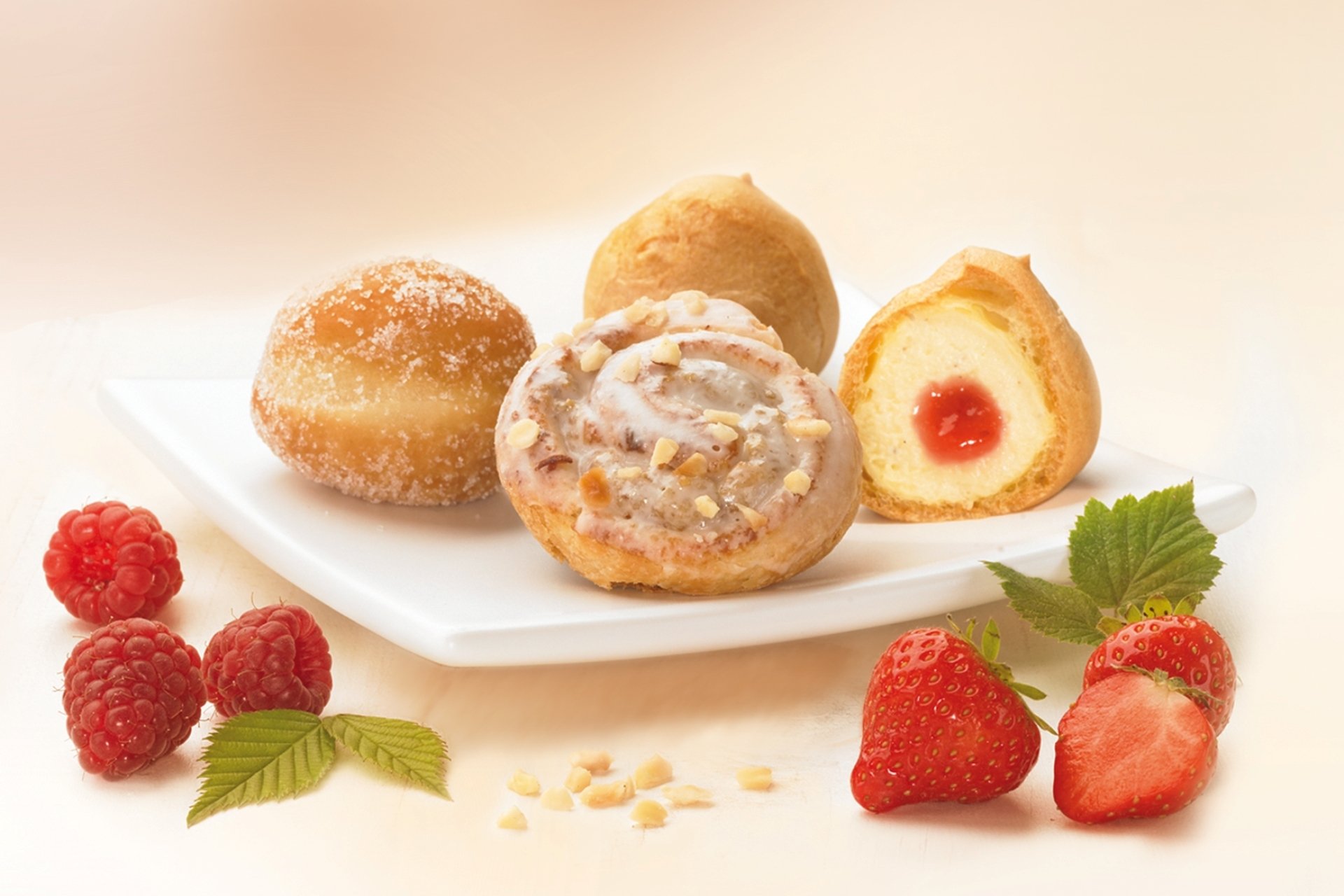 HD PC desktop wallpaper featuring assorted baked pastries, including cinnamon rolls and doughnuts, arranged with fresh strawberries and raspberries on a white surface.