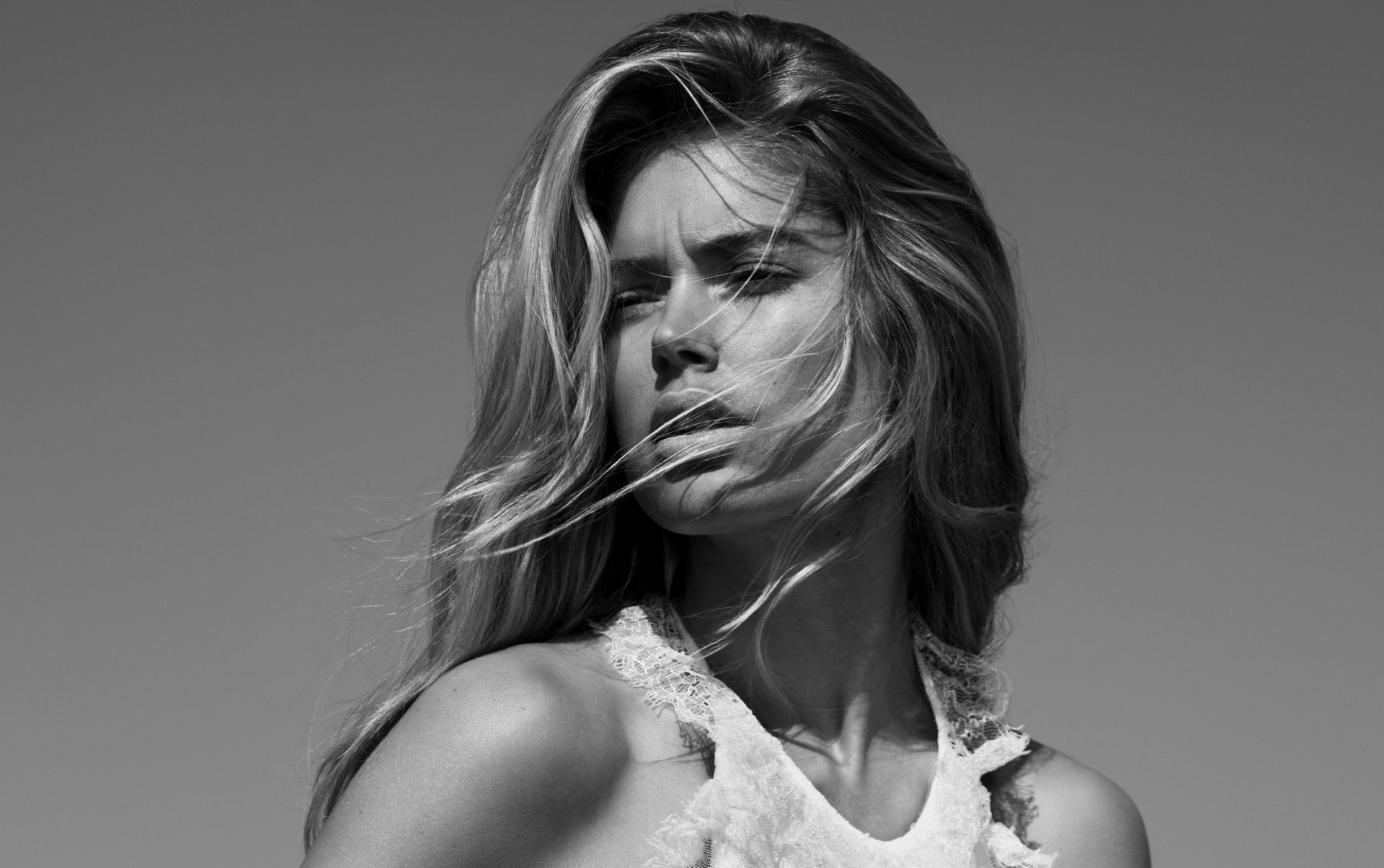 A striking black and white HD wallpaper featuring Doutzen Kroes, showcasing her beauty with wind-swept hair and a contemplative expression against a minimalist background.