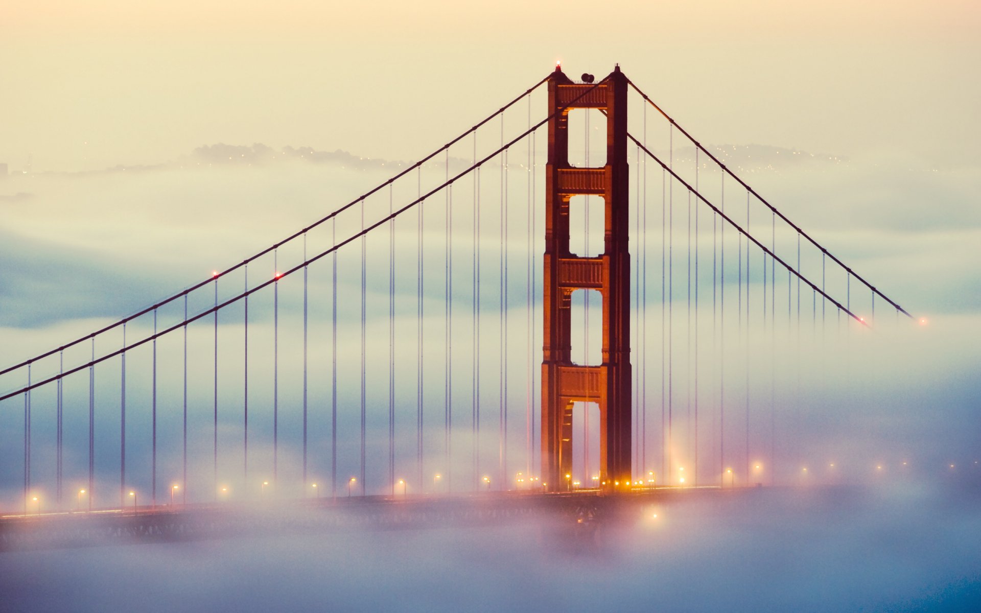 HD desktop wallpaper featuring the man-made Golden Gate Bridge rising through a layer of fog at dawn.