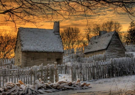 HD PC desktop wallpaper featuring a man-made rustic cabin with snow-covered roofs, surrounded by a wooden fence and leafless trees under a golden sunset sky.