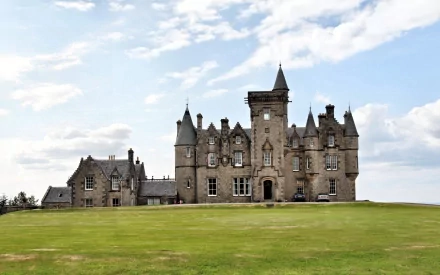 HD desktop wallpaper showcasing Glengorm Castle, a striking man-made historic stone structure set against a partly cloudy sky on a broad green lawn.