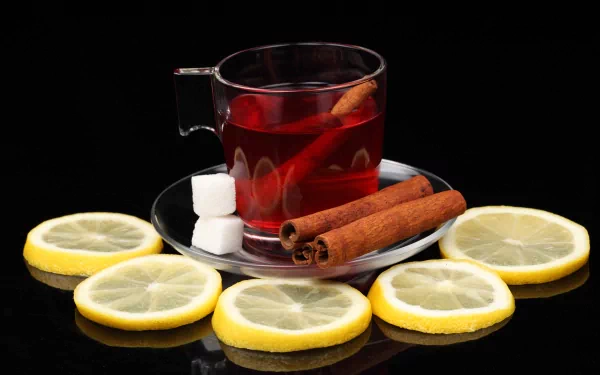 4K Ultra HD wallpaper featuring a glass cup of hot tea with cinnamon sticks, sugar cubes, and lemon slices arranged on a reflective black surface.