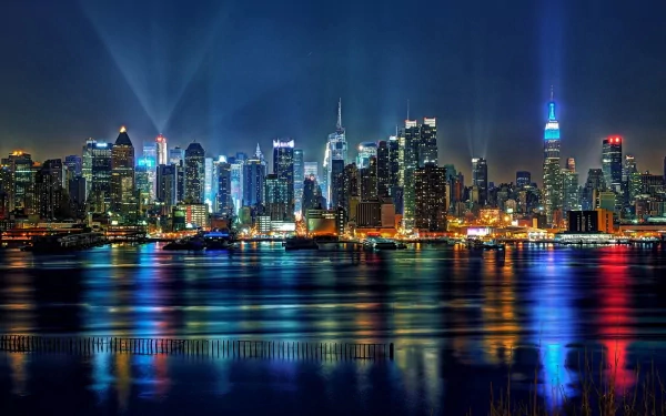 HD desktop wallpaper and background of the New York City skyline at night, showcasing brightly lit skyscrapers and their reflections on the water.