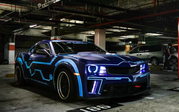 A striking Chevrolet Camaro parked in a dimly lit garage, featuring dynamic blue graphics and illuminated accents, makes for an eye-catching HD desktop wallpaper.