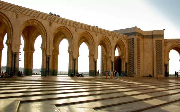 Sunlit arches and intricate architecture of Hassan II Mosque, captured in a HD image for a PC desktop wallpaper showcasing its religious and cultural grandeur.