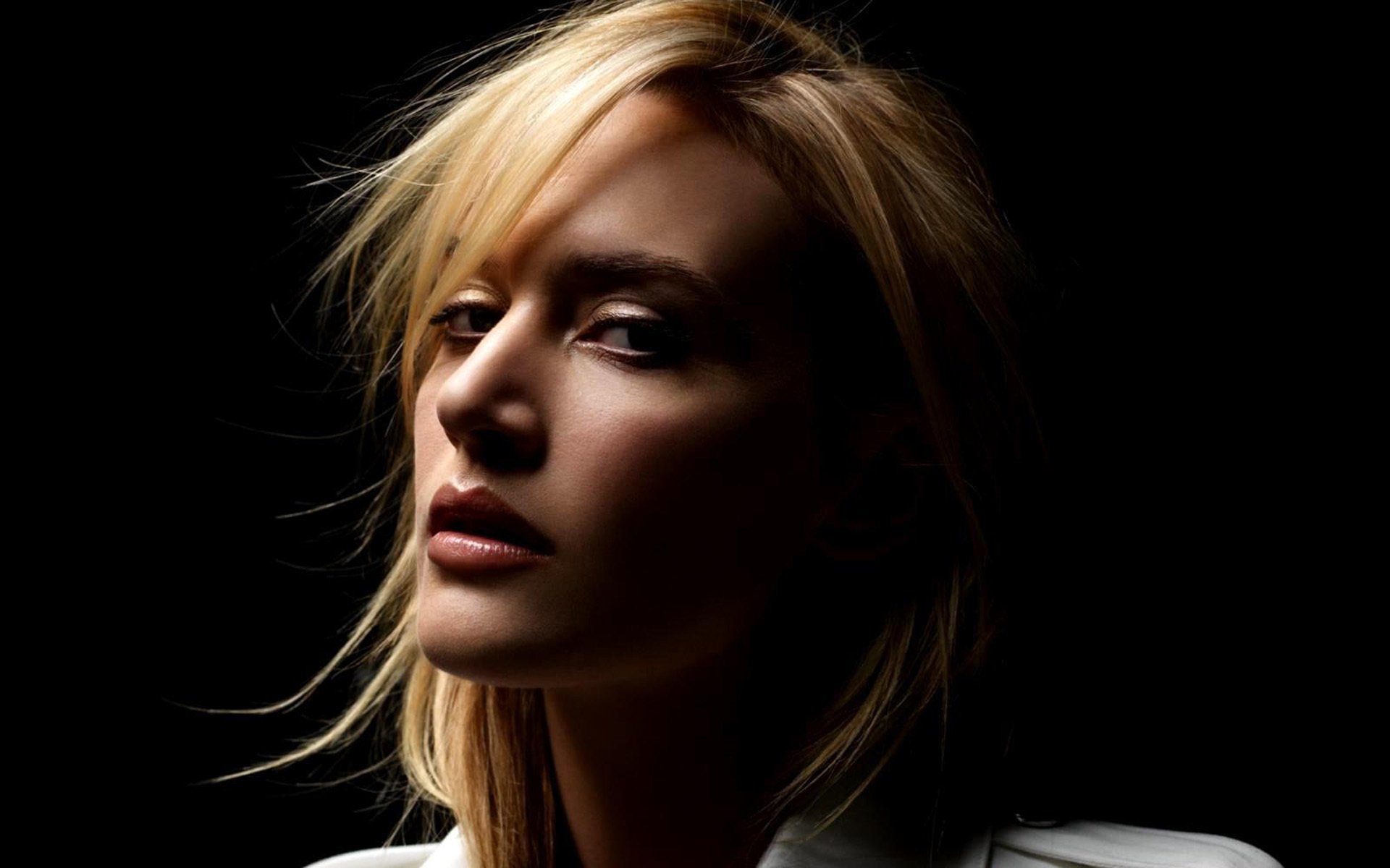 A striking HD wallpaper featuring Kate Winslet, showcasing her captivating features in a dramatic, low-light setting against a dark background.