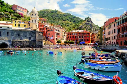 A vibrant view of Vernazza in Cinque Terre, Italy, showcasing colorful buildings, clear turquoise waters, and boats in the foreground, capturing the charm of this picturesque village.