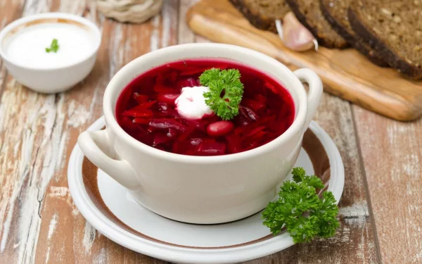 HD desktop wallpaper featuring a bowl of vibrant red soup garnished with sour cream and fresh parsley, accompanied by sliced bread on a rustic wooden table.