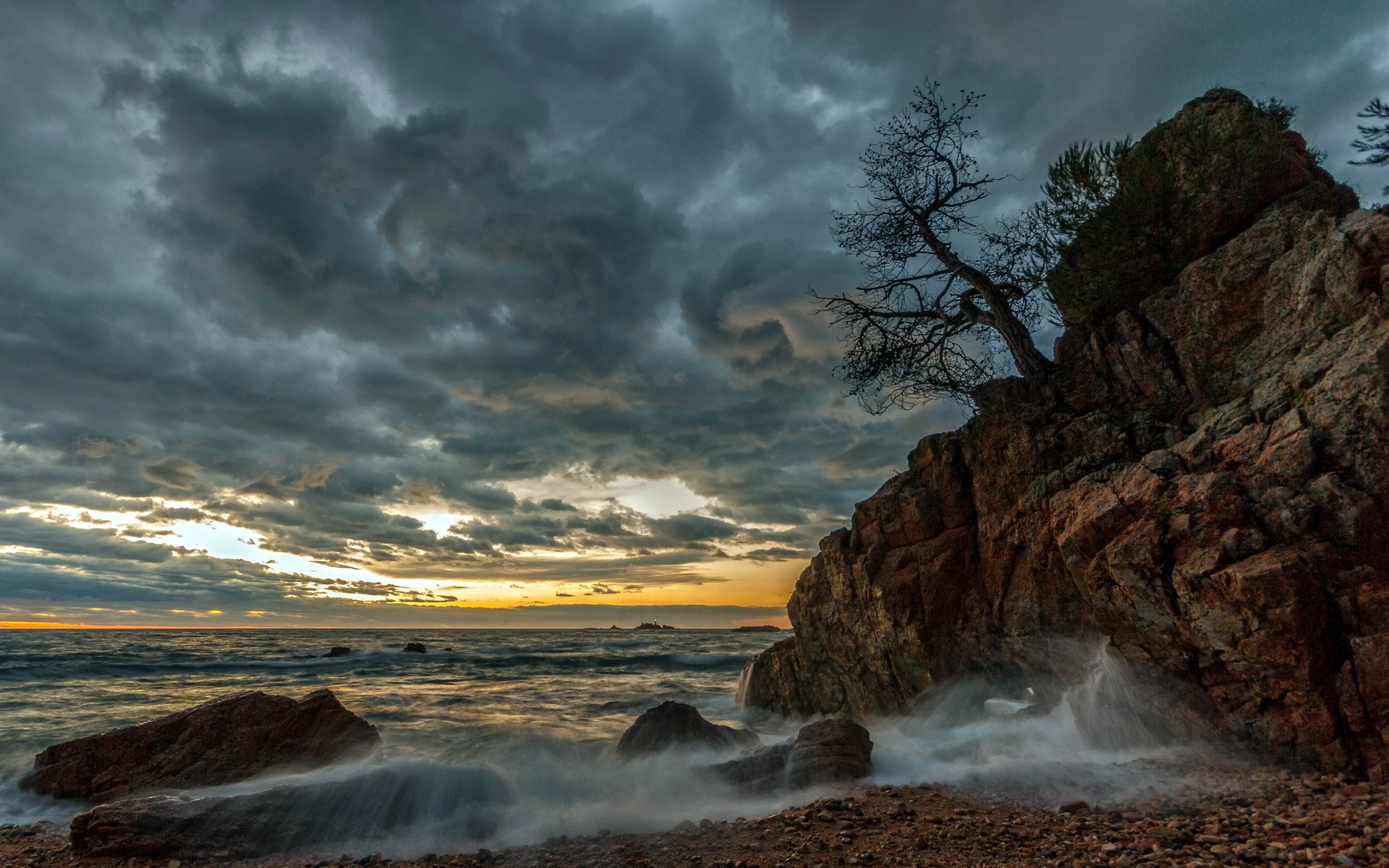HD PC desktop wallpaper featuring a dramatic nature scene with a rocky cliff, turbulent waves, and a cloudy sky at sunset.