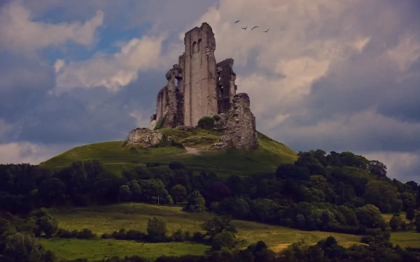 A breathtaking 4K Ultra HD image of a majestic ruin atop a hill, surrounded by lush greenery and dramatic clouds, offering a glimpse into man-made history against a natural backdrop.