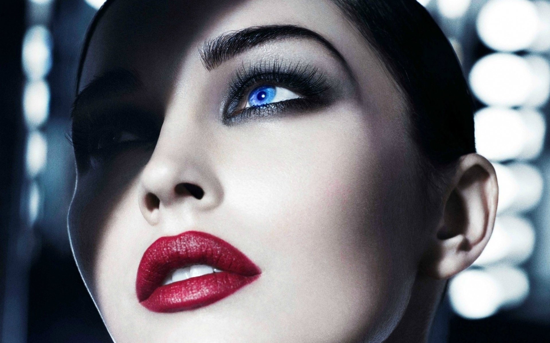 Close-up HD desktop wallpaper of a woman with striking blue eyes, bold red lips, and dramatic makeup, embodying the look of a model.