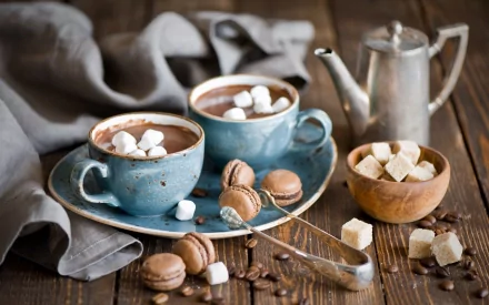 Still life HD desktop wallpaper featuring mugs of hot chocolate topped with marshmallows, surrounded by coffee beans, macarons, sugar cubes, and a teapot, set on a rustic wooden table.
