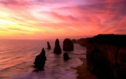 Sunset over the Twelve Apostles along Victoria's rugged coastline, with cliffs and ocean waves meeting under a vibrant sky.